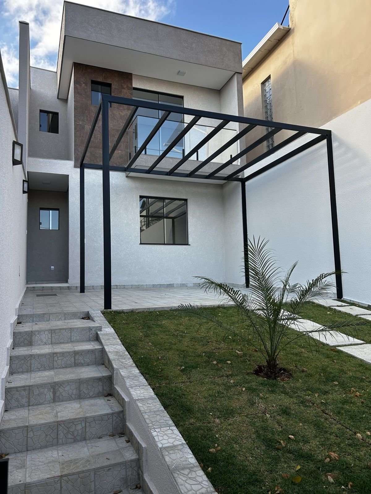 Fachada com pergolado metálico e jardim